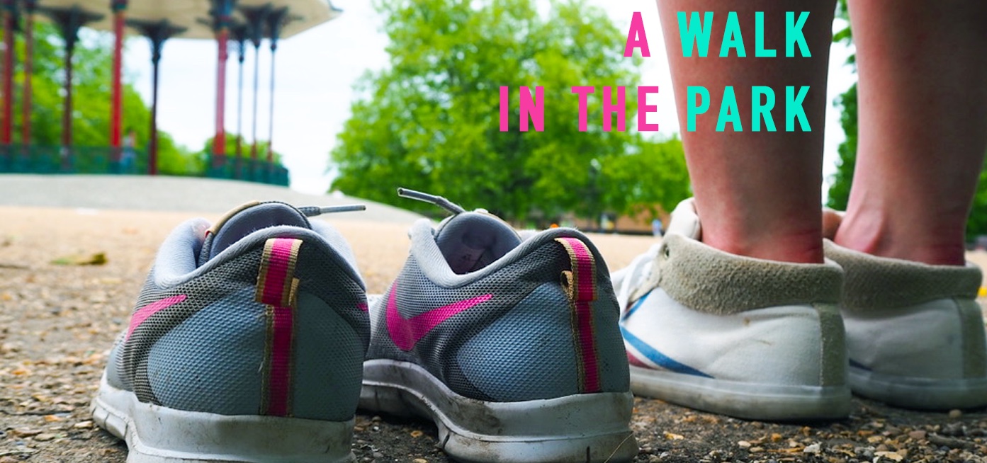 Promotional material for A Walk in the Park, two pairs of shoes. One of the pairs of shoes is empty, while someone is wearing the right hand pair. In the background there is a park and a bandstand.